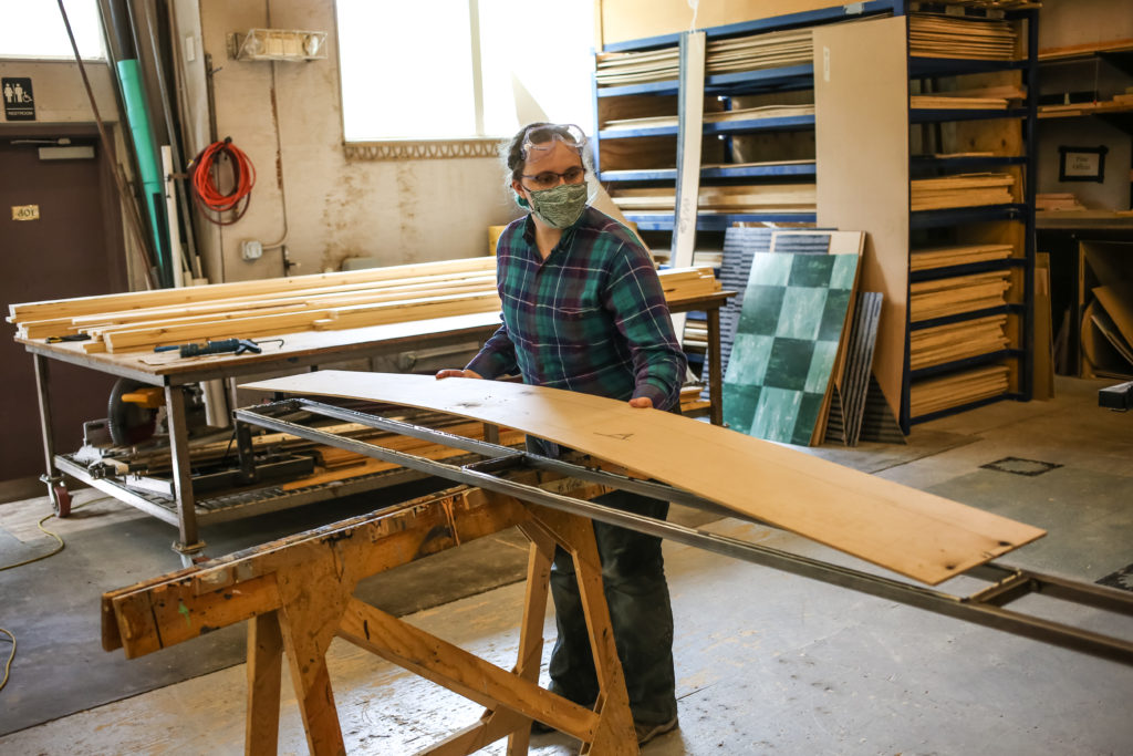 A person with teal hair places a piece of plywood on a steel frame.